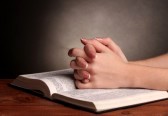 12144585-hands-folded-in-prayer-over-open bible